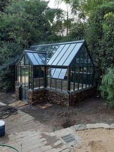 a small glass house sitting in the middle of a garden with lots of trees around it