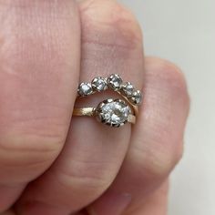 a person's hand holding a gold ring with two diamonds on it and the middle finger