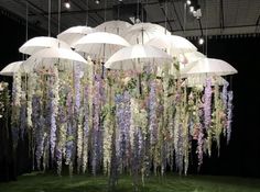 several white umbrellas hanging from the ceiling in front of purple flowers and greenery