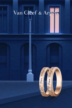 two gold wedding rings sitting in front of a building with the words van cleef & ampels written on them