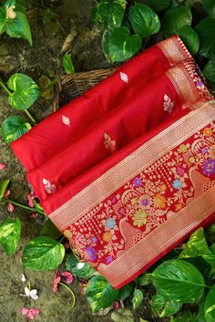 red and gold saree laying on the ground next to some green leafy plants