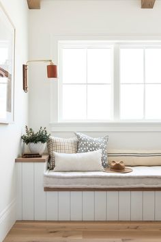 a window seat with pillows on it in front of a white wall and wooden floor