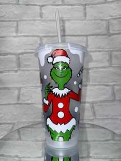 the grinch is wearing a santa hat and holding a straw in his hand while standing next to a brick wall