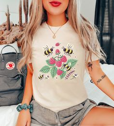 🐝 Buzz into Style with Our Bee Berries T-shirt! 🐝 Celebrate the sweetness of nature with our charming Bee Berries T-shirt. Perfect for lovers of bees and berries, this graphic tee combines the delightful imagery of honey bees and raspberries to create a cute and stylish addition to your wardrobe. Whether you're a fan of bumble bees or simply adore raspberries, this cotton tee is designed to make you stand out. Featuring a playful design that captures the essence of nature's harmony, this bee a Cute Short Sleeve T-shirt With Plant Print, Cute Crew Neck T-shirt With Plant Print, Bumble Bee Cute, Fruit T Shirt, Bee Cute, Bumble Bees, Honey Bees, Shirts For Women, Honey Bee