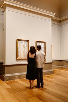 a man and woman looking at paintings on display in an art gallery with hard wood flooring