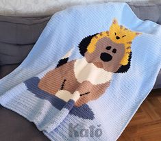 a crocheted blanket with a dog on it sitting on a couch next to a pillow