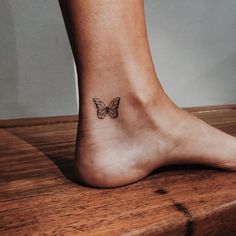 a small butterfly tattoo on the foot of a woman's right leg, which is sitting on top of a wooden table