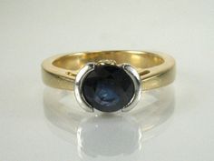 Up for sale is a lovely estate sapphire ring crafted in 7 grams of 18K yellow gold with a platinum head. The sapphire is round faceted measuring 6.19 x 6.22 mm and weighing an estimated 0.93 carats. It's a deep blue stone, lightly included, and shows neatly in the half bezel platinum setting. Two fine round brilliant cut diamonds add a nice touch, small yet sparkly stones graded H-I color, VS1-VS2 clarity and weighing an estimated 0.02 carats combined. The styling is more contemporary and the ri Modern Yellow Gold Sapphire Ring With Center Stone, Formal Yellow Gold Sapphire Ring With Tension Setting, Yellow Gold Sapphire Ring With Tension Setting, Formal Round Sapphire Ring With Tension Setting, Modern Gold Sapphire Ring With Center Stone, Sapphire Solitaire Engagement Ring, Engagement Ring Types, Diamond Ring Engagement, Antique Bridal Jewelry