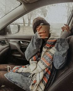 a woman sitting in the passenger seat of a car holding a coffee cup and looking at her cell phone