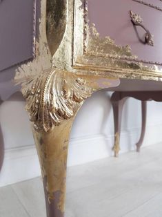 an ornate gold and purple dresser with mirror on it's side, next to a white wall