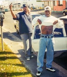 two men standing in front of a white car with graffiti on the chest and arms