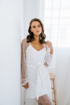 Our most luxurious robe yet. Luxe tulle is encrusted with faux pearl detailing which delicately flows across the body. The romantic billowing sleeves have an elasticised cuff, and the robe is tied at the front with a waistband. Our pearl encrusted robe is perfect for the bride and those getting ready photos. Sold with a white cami slip. PRE ORDER - Early Jan arrival Details: Pearl tulle maxi robe overlay Matte white satin slip included White waist tie Elasticised cuffs Exclusive to Miss Poppy De Pearl Bridal Robe, Poppy Design, White Bride, White Cami, Bride Getting Ready, White Slip, Bridal Robes