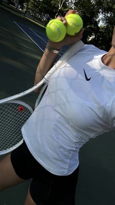 a woman holding two tennis balls on top of a tennis court with her racquet