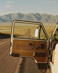 the driver's door is open on an empty road with mountains in the background