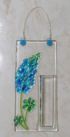 a piece of glass with blue flowers and green leaves on it, hanging from a wall