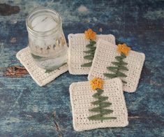 three crocheted coasters with small trees on them next to a glass jar