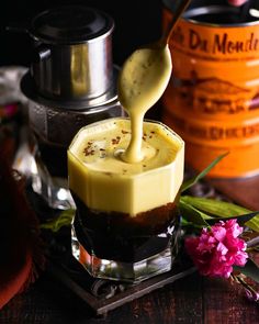 a spoon drizzling something into a cup filled with liquid on top of a table