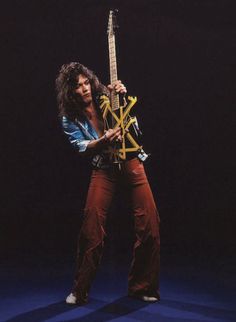 a man with long hair holding an electric guitar in his right hand and posing for the camera