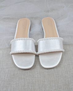 a pair of white slippers with pearls on the bottom and straps, sitting on a bed