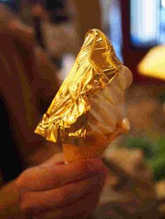 a person holding up a piece of food wrapped in tin foil on top of a table