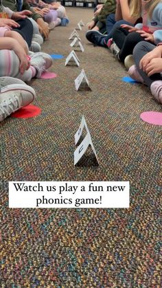 a group of kids sitting on the floor playing a game with paper airplanes in front of them