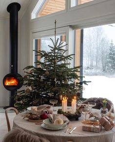 a dining room table with a christmas tree in the center and candles on it next to an open fire place