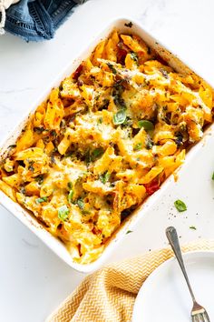 a casserole dish with cheese and vegetables in it next to a fork on a plate