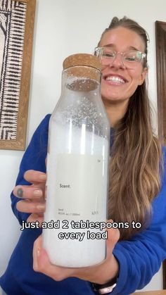 a woman is holding a large jar full of milk and smiling at the camera with text overlay that reads just add 2 tablespoos to every load