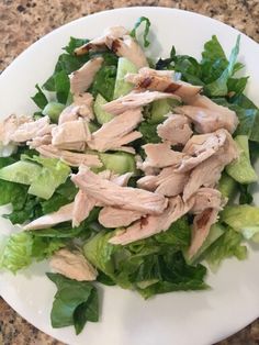 a salad with chicken and lettuce on a white plate sitting on a granite countertop