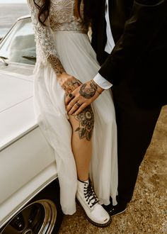 a man and woman standing next to each other in front of a car with tattoos on their arms