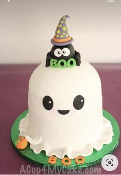 a cake with a ghost on top and a hat on it's head is sitting on a purple surface