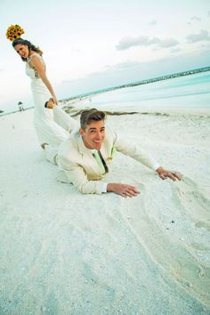 a man and woman are laying on the beach in their wedding attire, posing for a photo