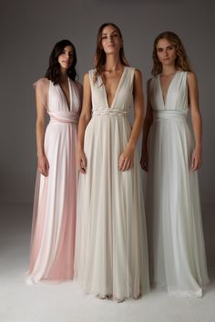 three women standing next to each other in long white and pink gowns, one wearing a v - neck dress