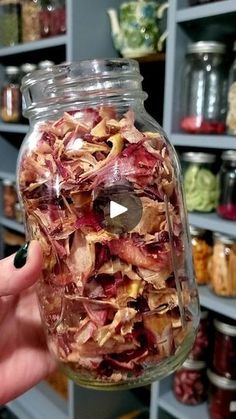 a person holding up a jar full of food in front of shelves filled with jars