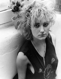 a black and white photo of a woman leaning against a wall with her hair blowing in the wind