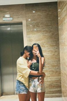 a man and woman standing in front of an elevator taking a selfie with their cell phone