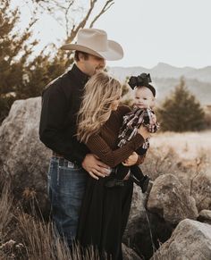 a man and woman holding a baby in their arms while standing next to some rocks