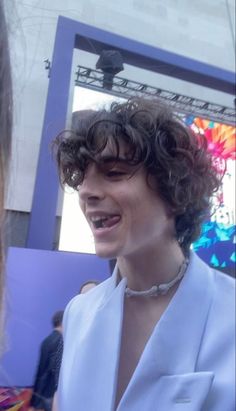 a woman with curly hair wearing a white suit and smiling at someone in the background