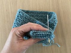 a hand holding a knitting needle next to a crocheted square