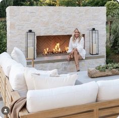 a woman sitting in front of an outdoor fireplace