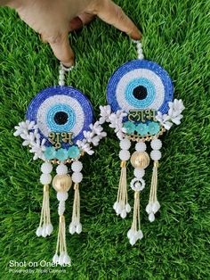 two blue and white earrings on grass with one being held up to the side by someone's hand