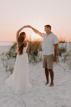 a man and woman standing on top of a sandy beach