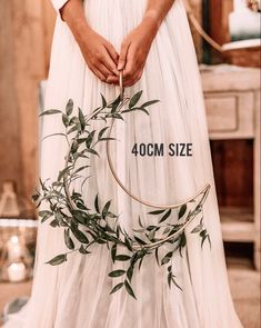 a woman in a white dress holding a hoop with greenery on it and the words, 40cm size