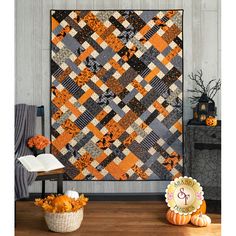 an orange and black quilt hanging on the wall next to a basket with flowers in it