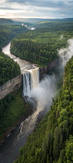 an aerial view of a waterfall in the middle of a forest with mist coming from it