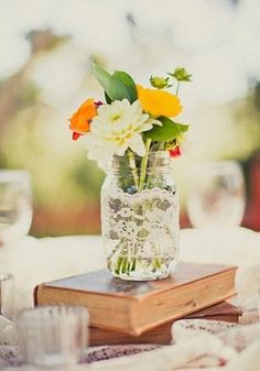 a vase filled with flowers sitting on top of a table next to books and glasses