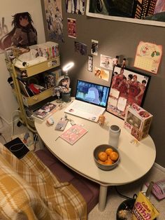 a desk with a laptop, monitor and oranges on it in front of a bed