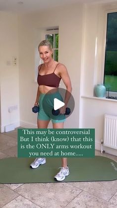 a woman standing on top of a green mat in front of a window holding two dumbbells