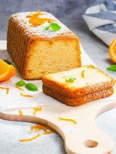 a loaf of orange pound cake on a cutting board next to an orange slice and some leaves