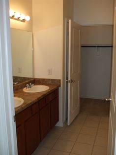 an empty bathroom with two sinks and a door leading to another room that has a closet on the other side